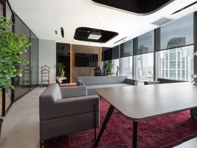Gri koltuklu, desenli halılı özel ofis oturma köşesi, ahşap aksan duvar ve şehir manzaralı cam cephe